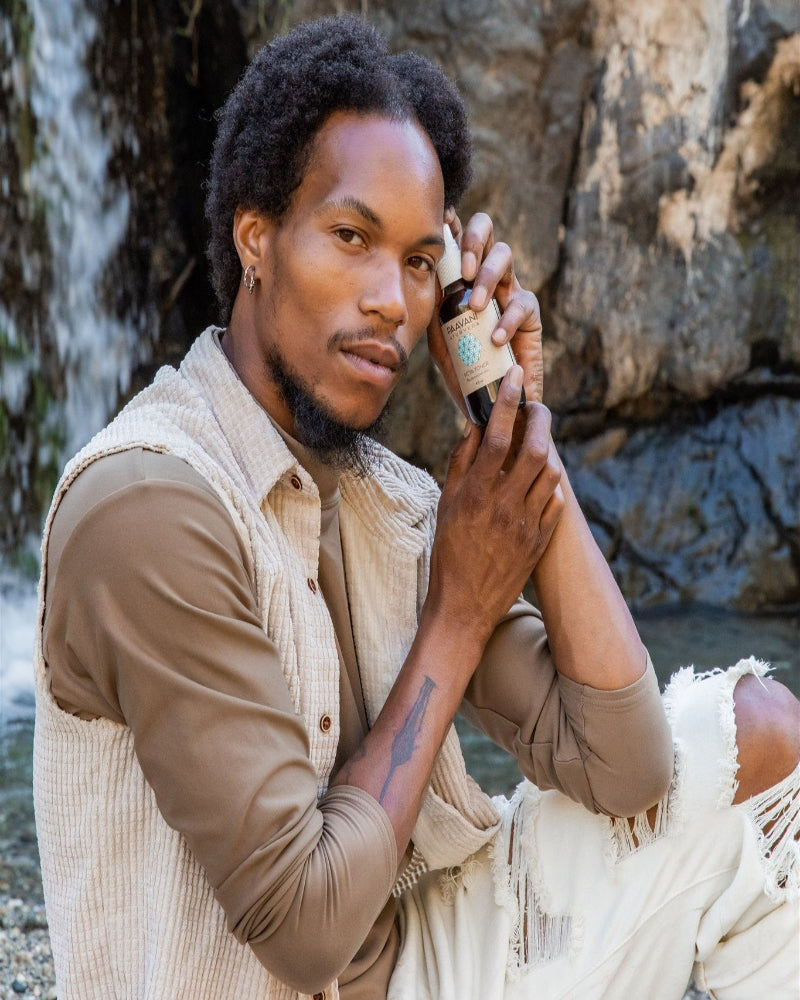 Man holding skincare products outdoors with a natural background