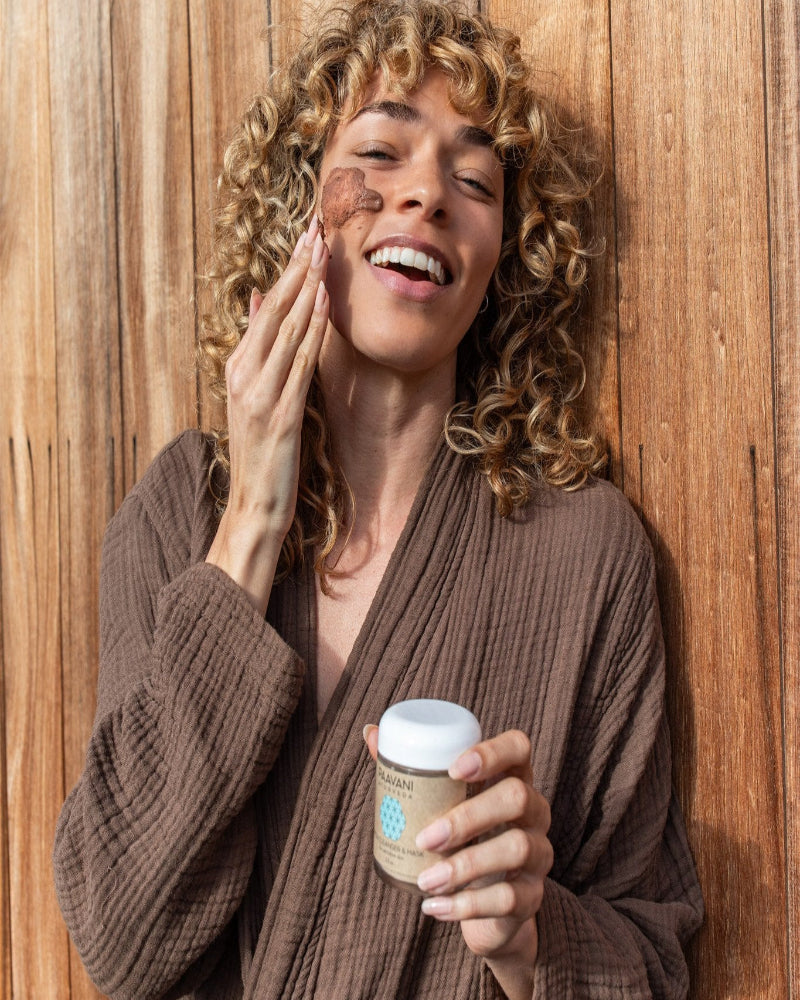 Woman applying cream to her face with a wooden background