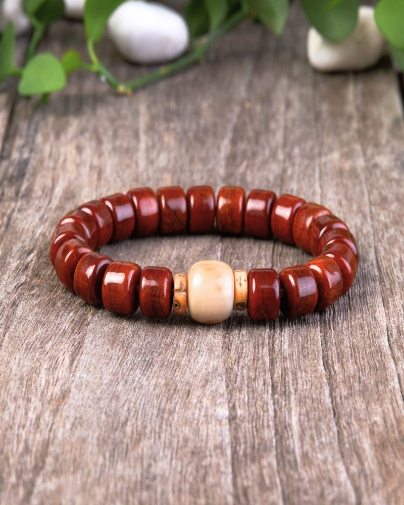Red beaded bracelet with a central beige bead on a wooden surface