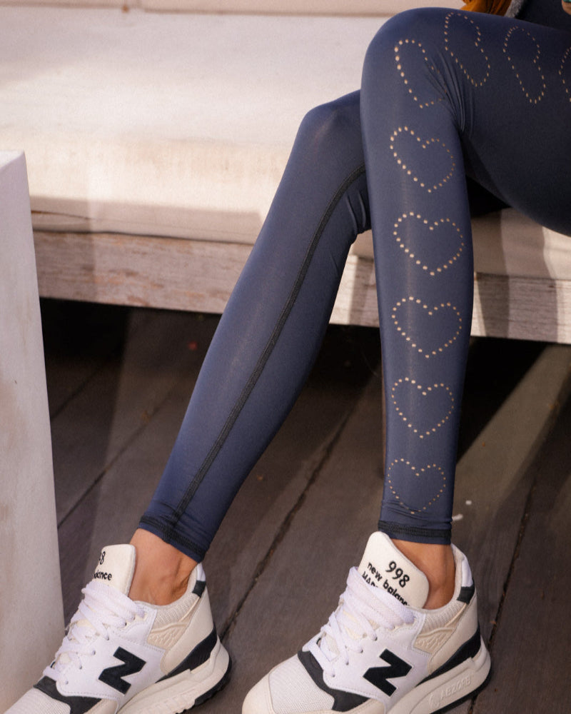 Person wearing blue leggings with heart patterns and white sneakers sitting on a bench.