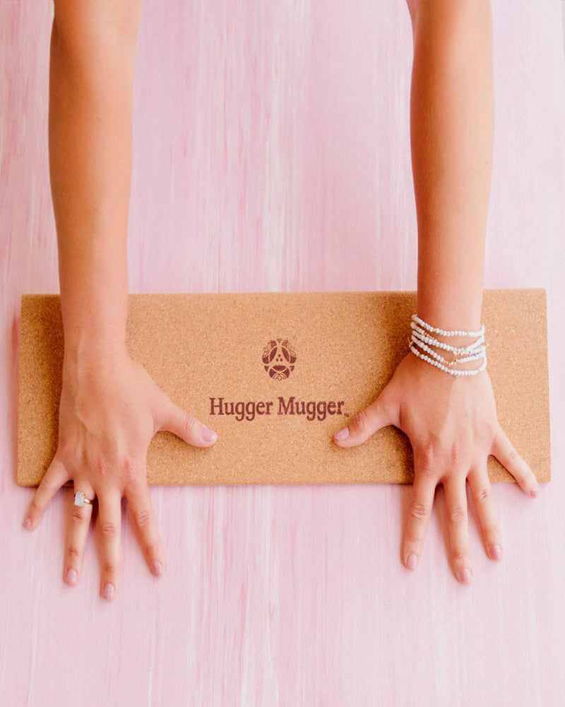 Cork yoga mat with 'Hugger Mugger' branding on a pink background