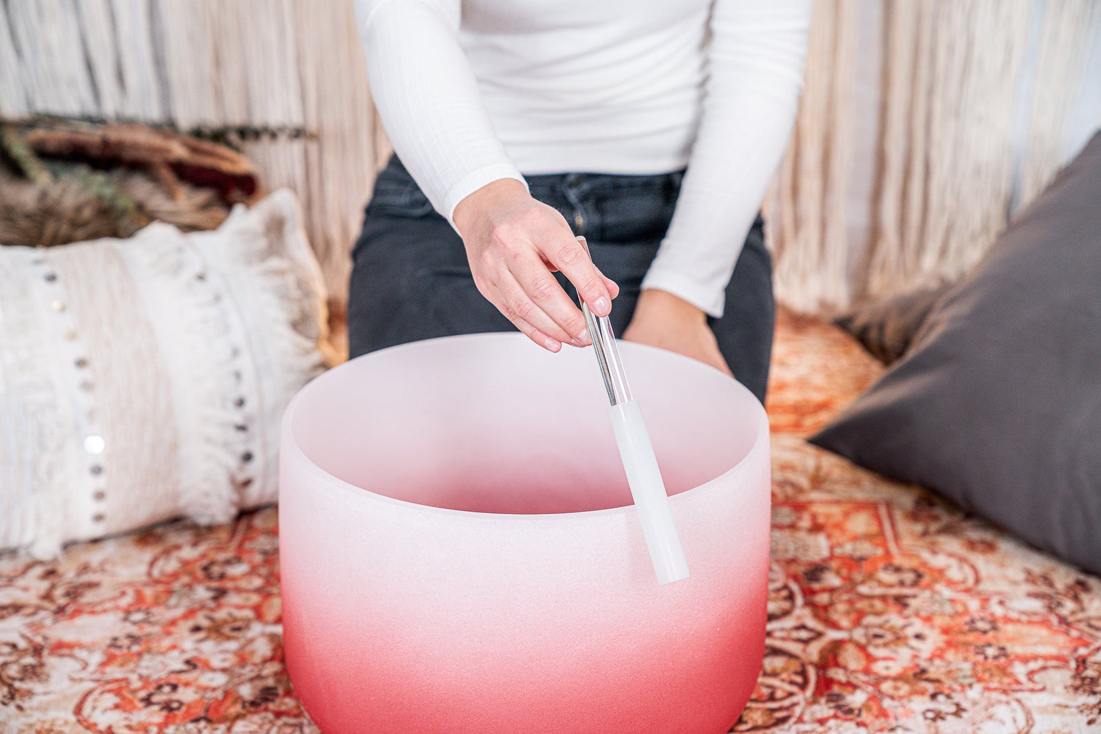 Person holding a tuning fork over a pink singing bowl on a patterned rug.