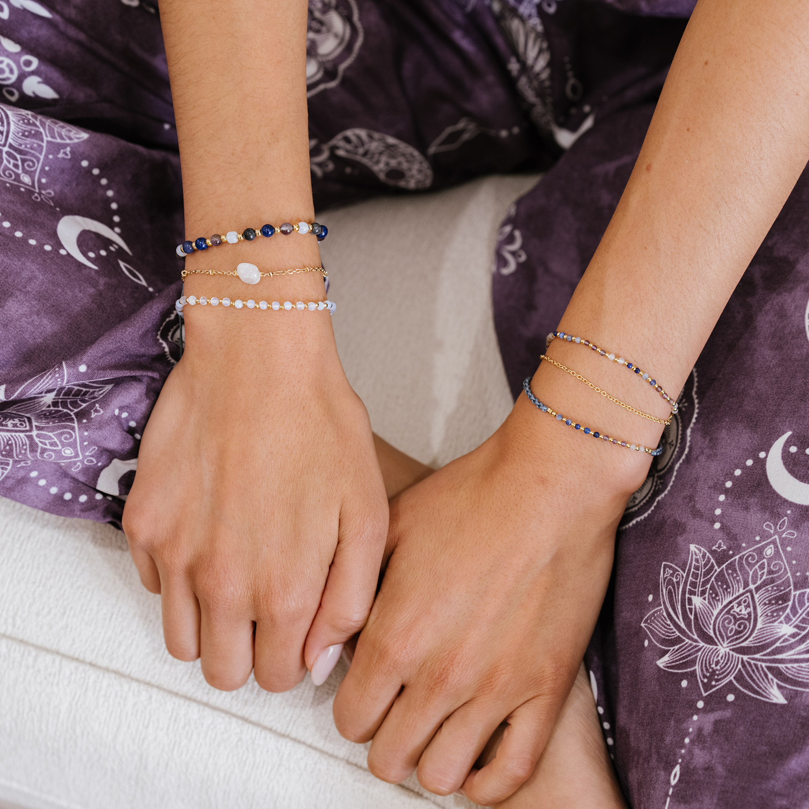 Close-up of hands wearing multiple bracelets on a purple fabric background with moon and star patterns.