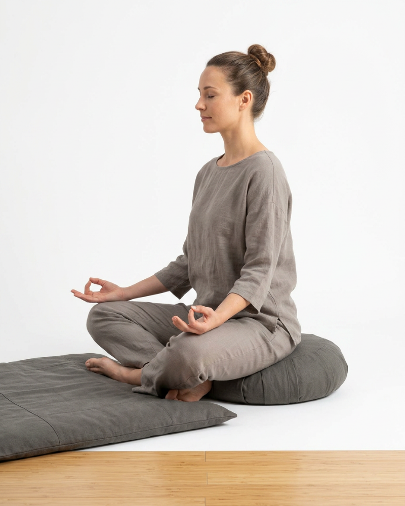 Woman sitting in a yoga pose on a gray mat with a white background