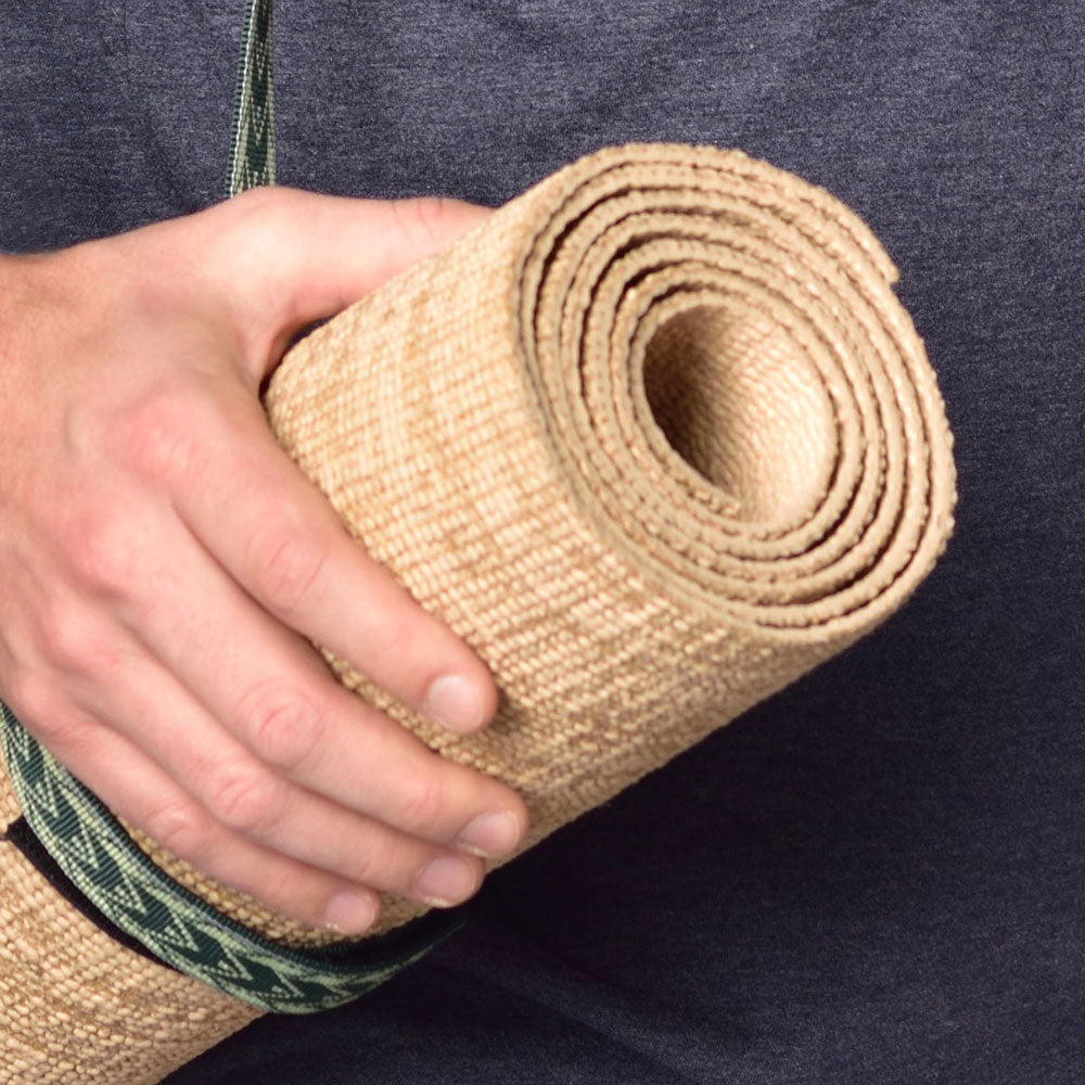 Hand holding a rolled-up beige yoga mat with a dark background