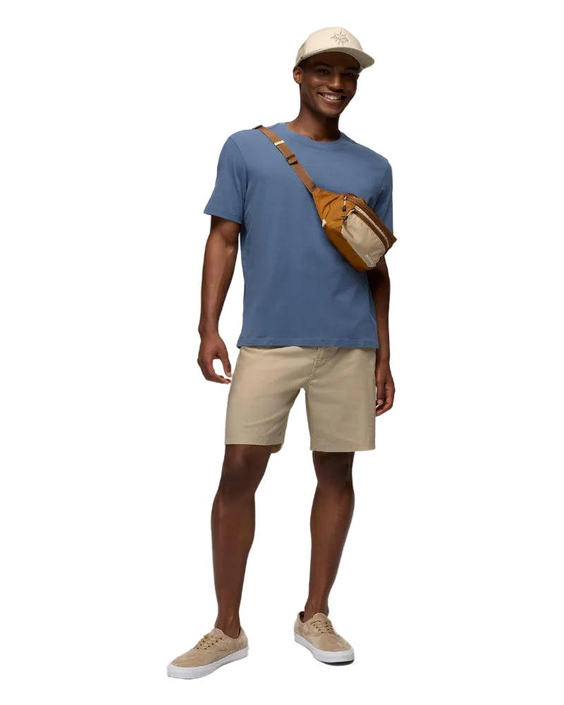 Man wearing a blue t-shirt, beige shorts, and a cap, standing against a white background.