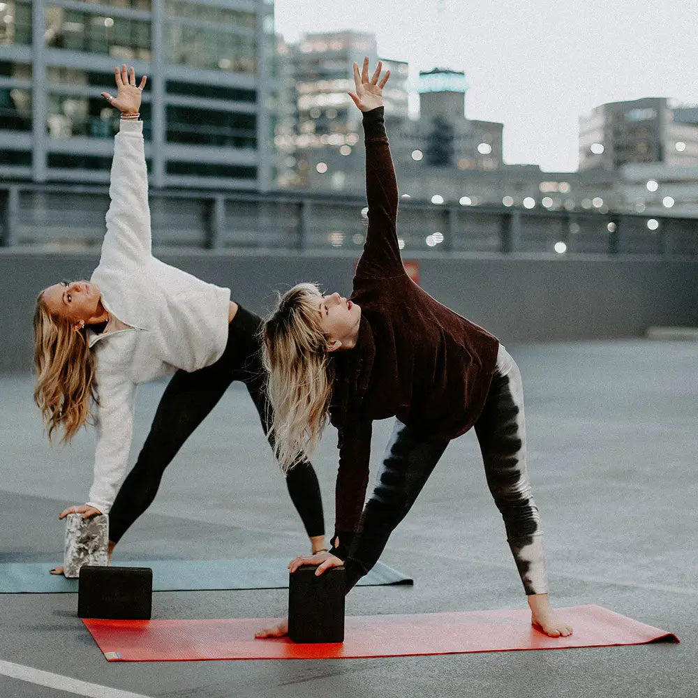 Two women practicing yoga on a rooftop with cityscape in the background