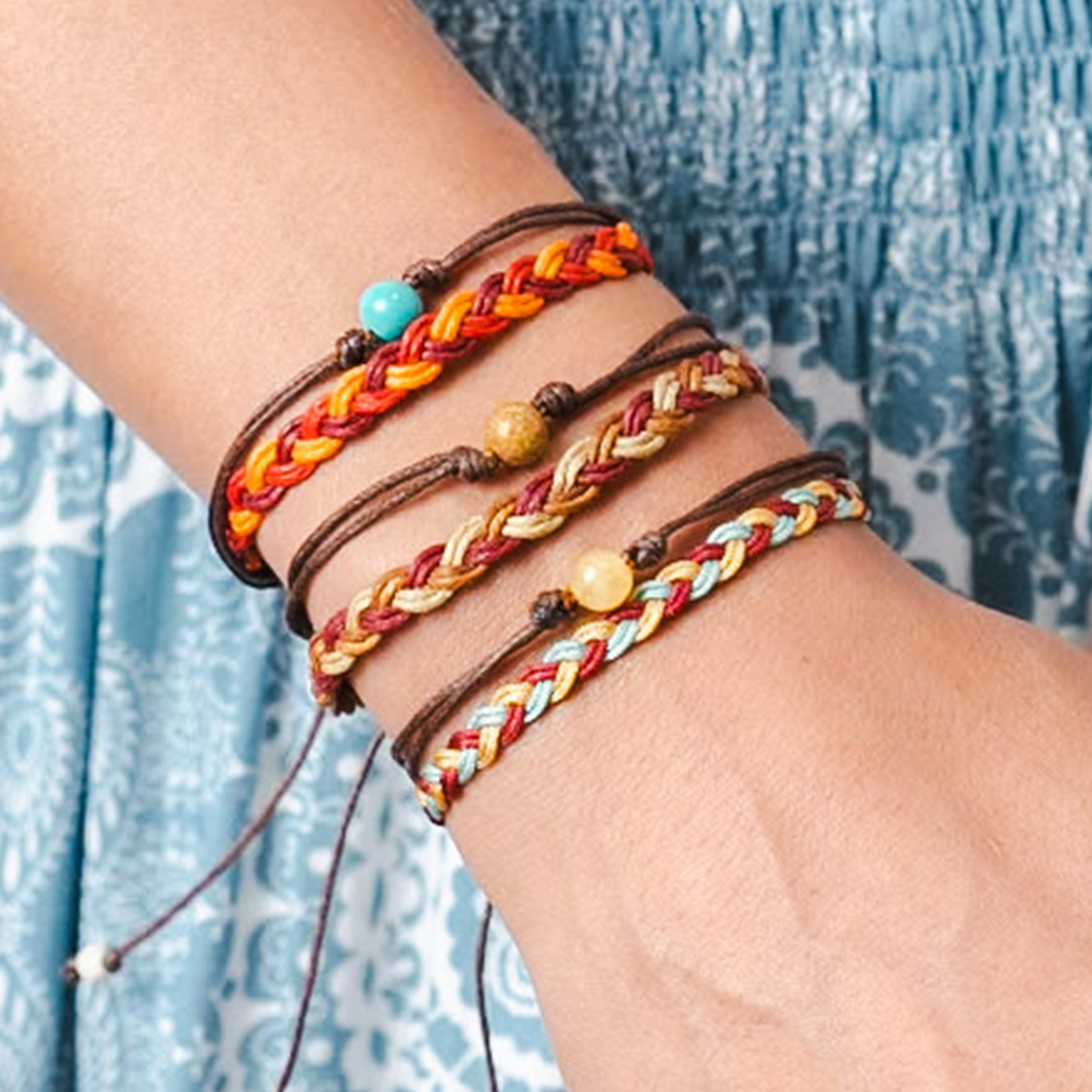 Multicolored braided bracelets on a wrist with a blue patterned fabric background