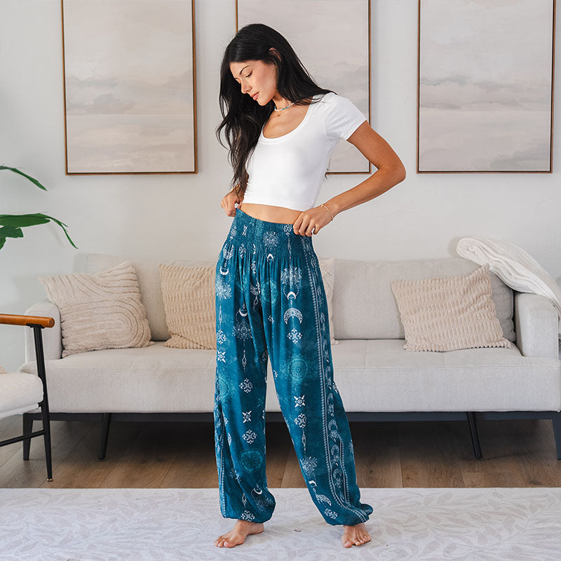 Woman wearing teal patterned pants and a white top in a living room.