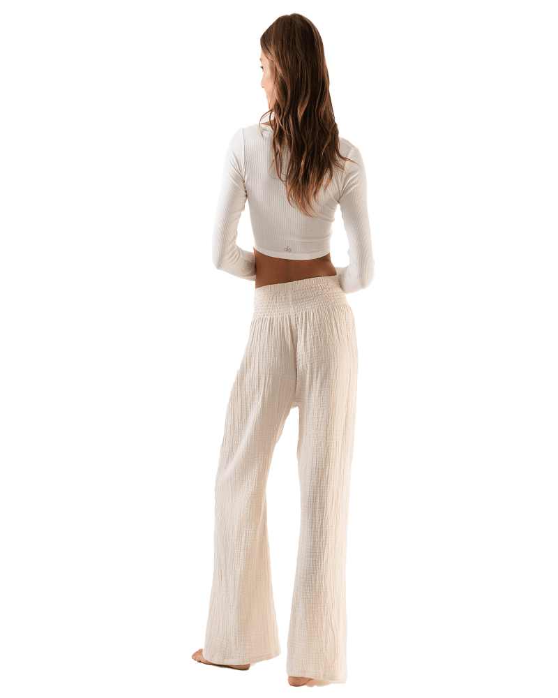 Woman wearing a white long-sleeve top and beige wide-leg pants on a white background