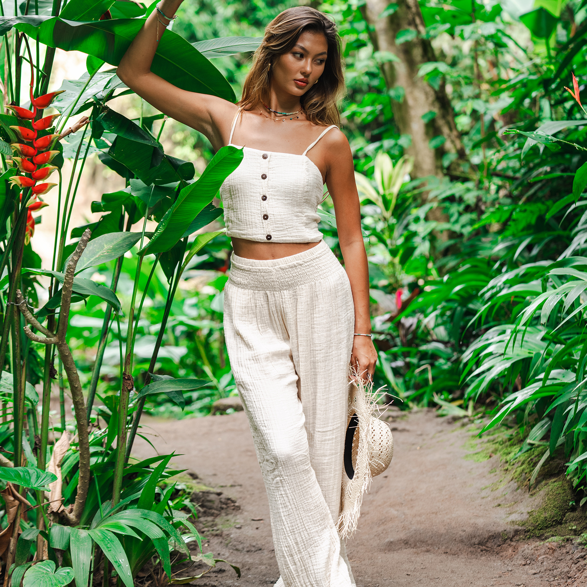 Woman in a white outfit walking through a lush tropical garden