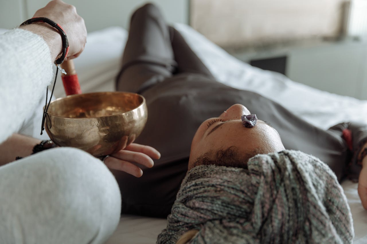 Person lying on a massage table with a therapist holding a singing bowl in a spa setting.