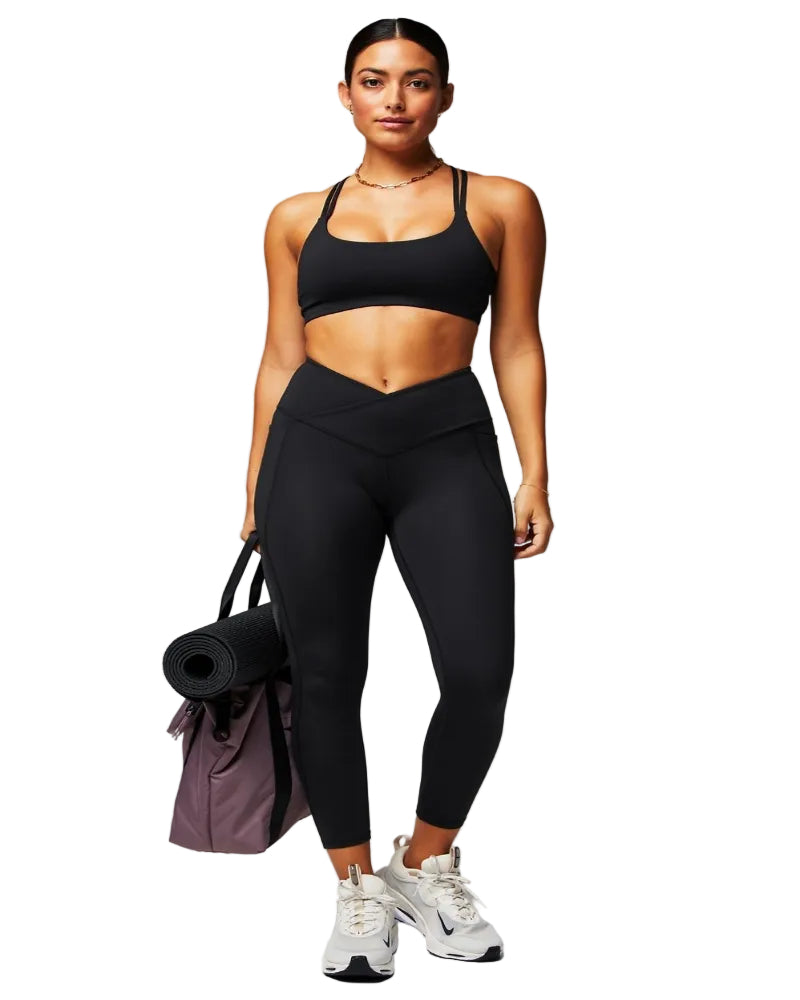 Woman in black athletic wear holding a yoga mat on a gray background