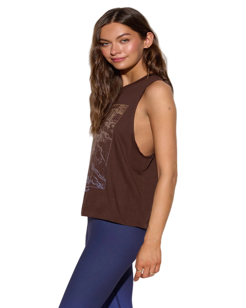 Woman wearing a brown sleeveless top with a graphic design and blue leggings on a white background