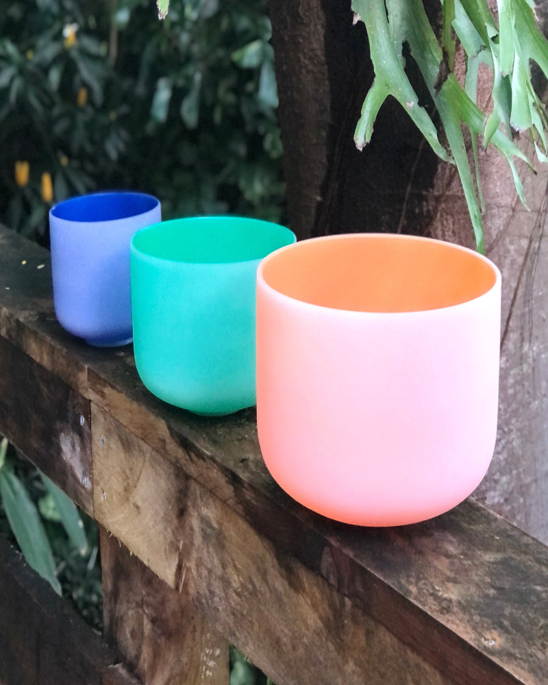 Three colorful bowls (blue, green, pink) on a wooden surface with a natural background.