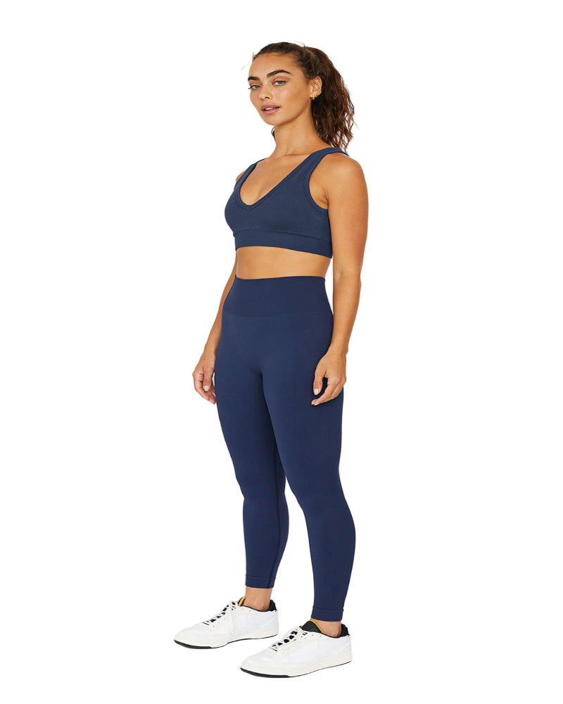 Woman wearing a navy blue sports bra and leggings set on a white background