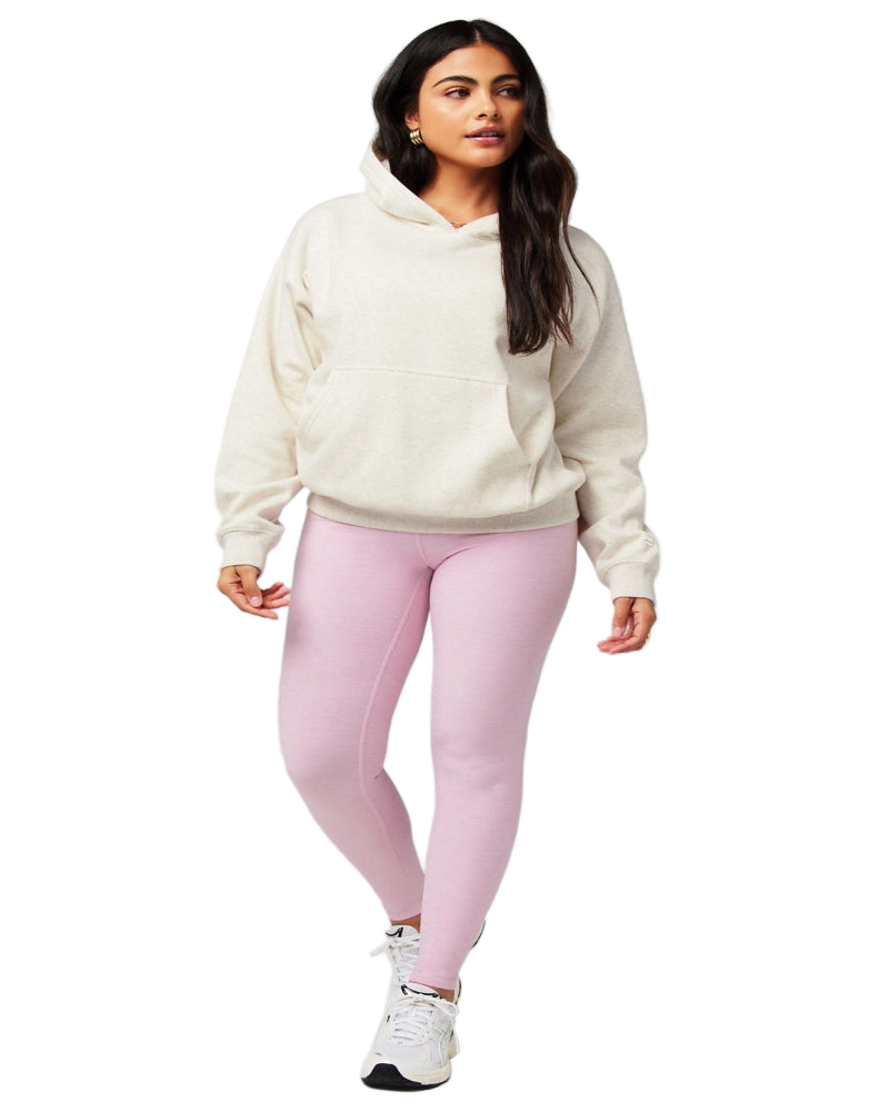 Woman wearing a cream hoodie and pink leggings on a gray background