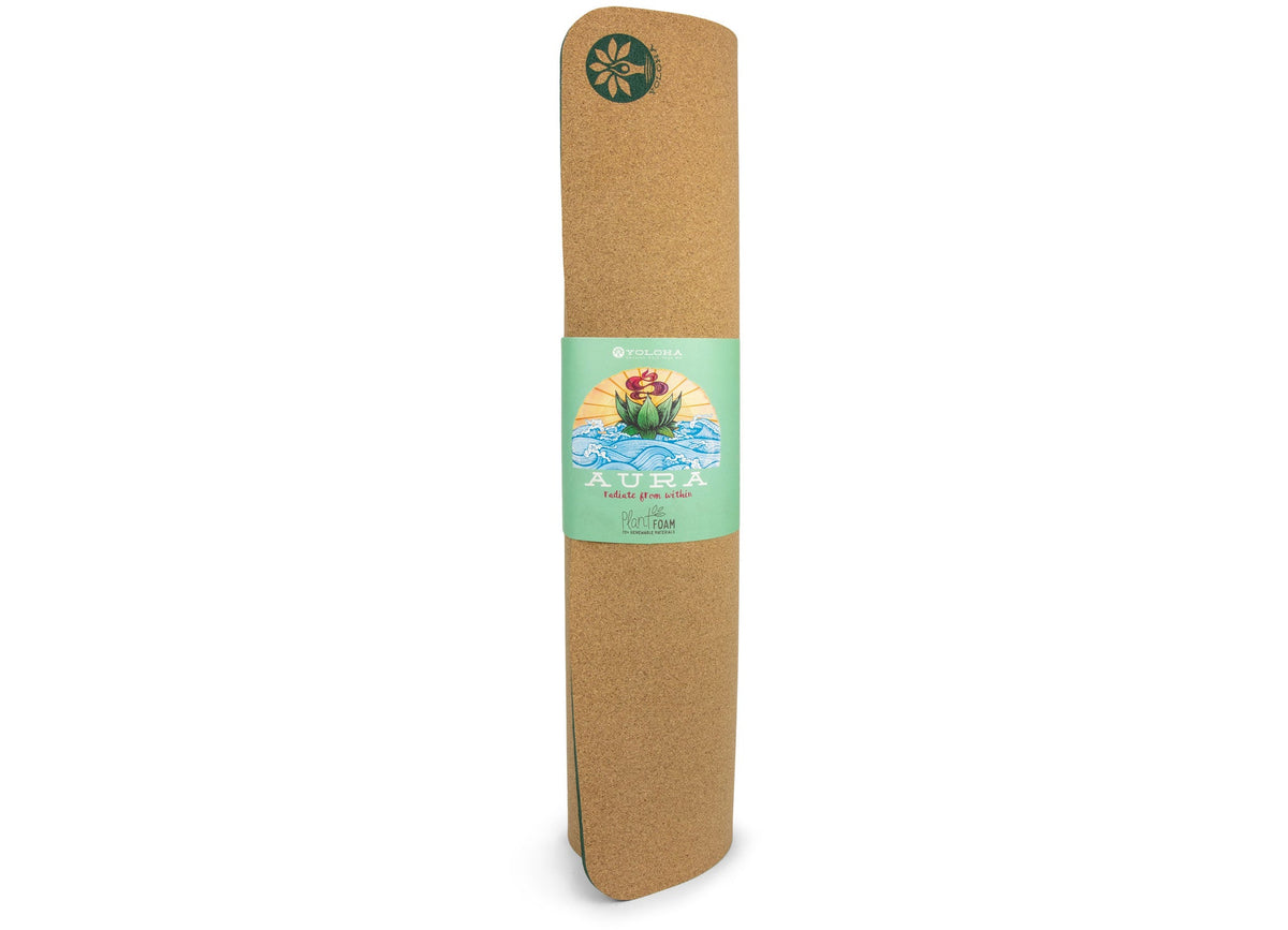 A rolled-up natural cork yoga mat with a mint green paper band around the middle. The band features a colorful illustration of a lotus flower and the brand name 'ACURA'.