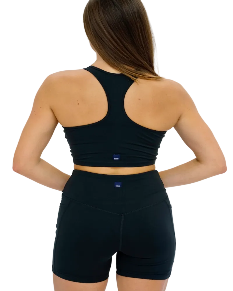 A woman wearing a black V-neck sports bra top with a front cut-out and backless design, paired with black activewear pants.