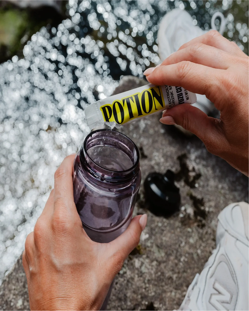Person holding a jar with a tube labeled 'POTION' against a blurred natural background