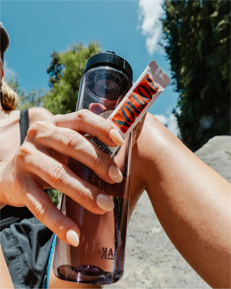 Two people holding a bottle with a 'NOTION' label outdoors on a sunny day.