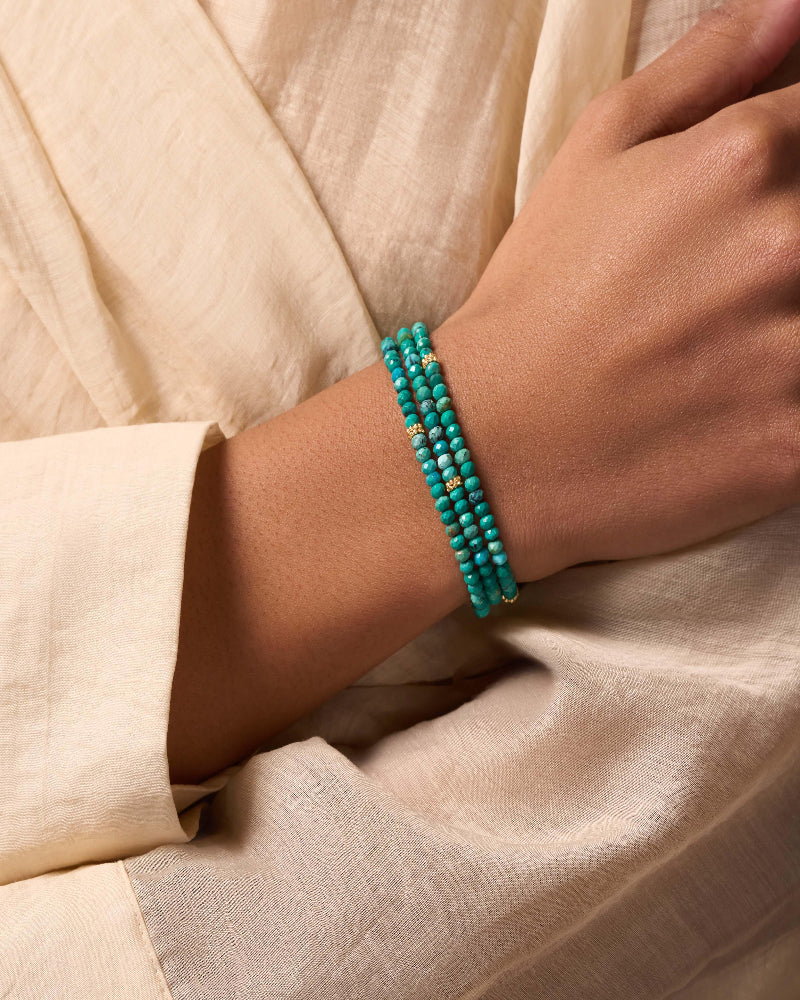 Turquoise beaded bracelet on a wrist with a beige fabric background