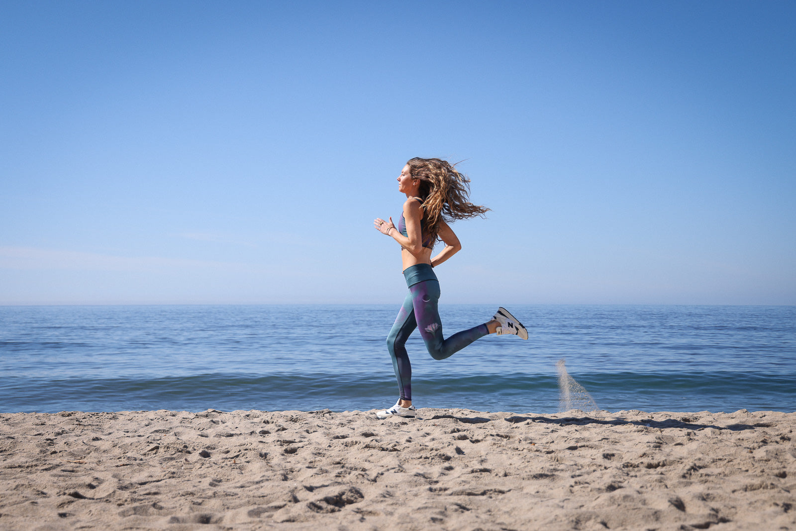 Woman running on a sandy beach with ocean and clear blue sky in the background
