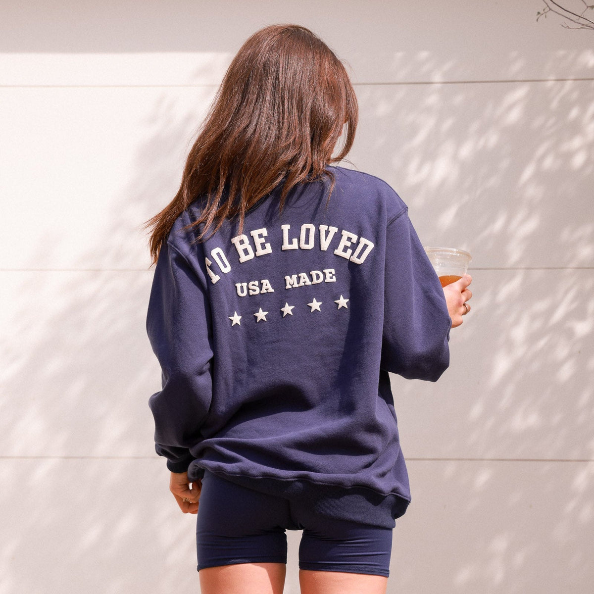 Person wearing a navy blue sweatshirt with text, holding a drink against a light background