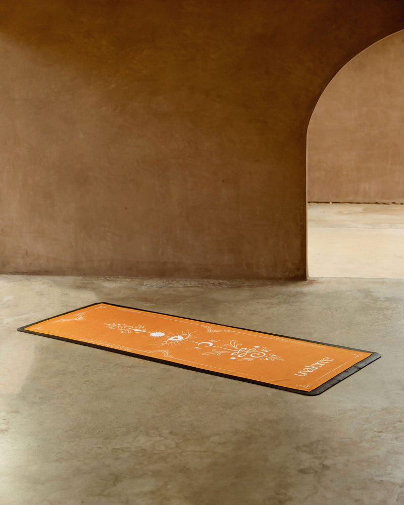 Orange yoga mat with branding on a concrete floor against a brown wall.