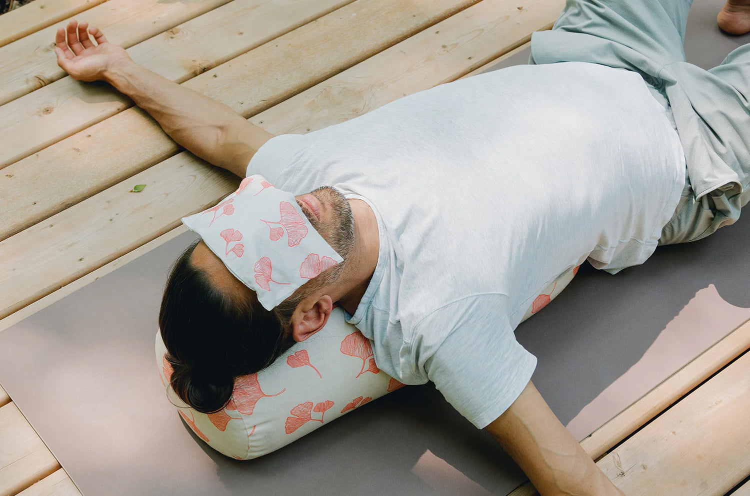 Person lying on a yoga mat with a pillow and eye mask on a wooden deck