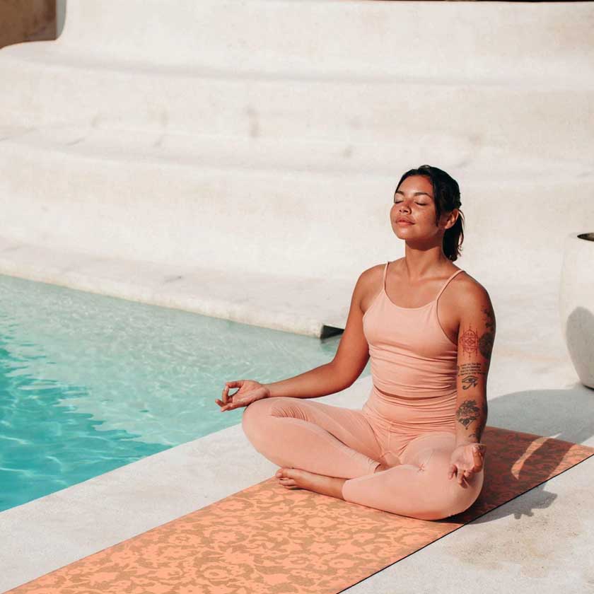 Woman in peach outfit meditating on a mat by a pool