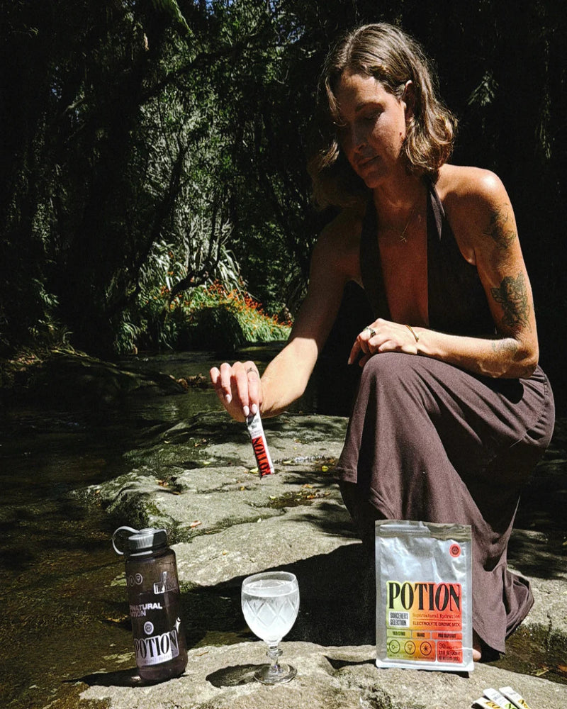 Person sitting by a stream with a bottle labeled 'Potion' and a glass.