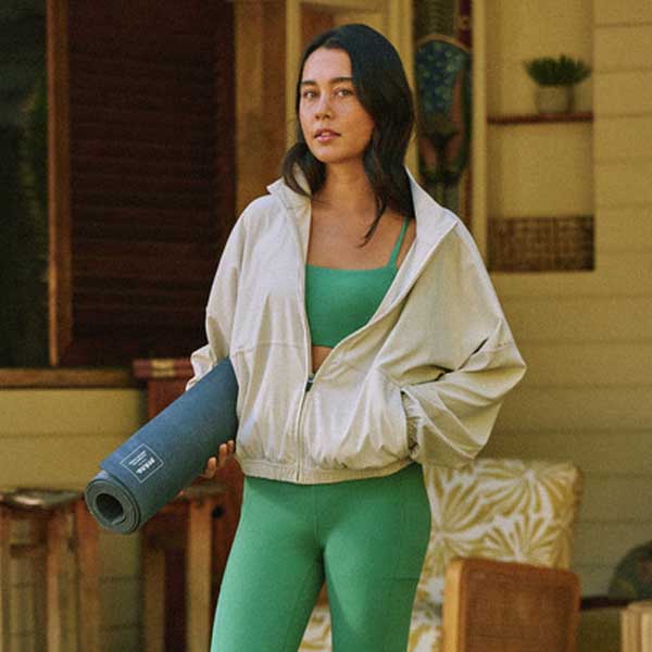 Woman in green athletic wear holding a yoga mat indoors