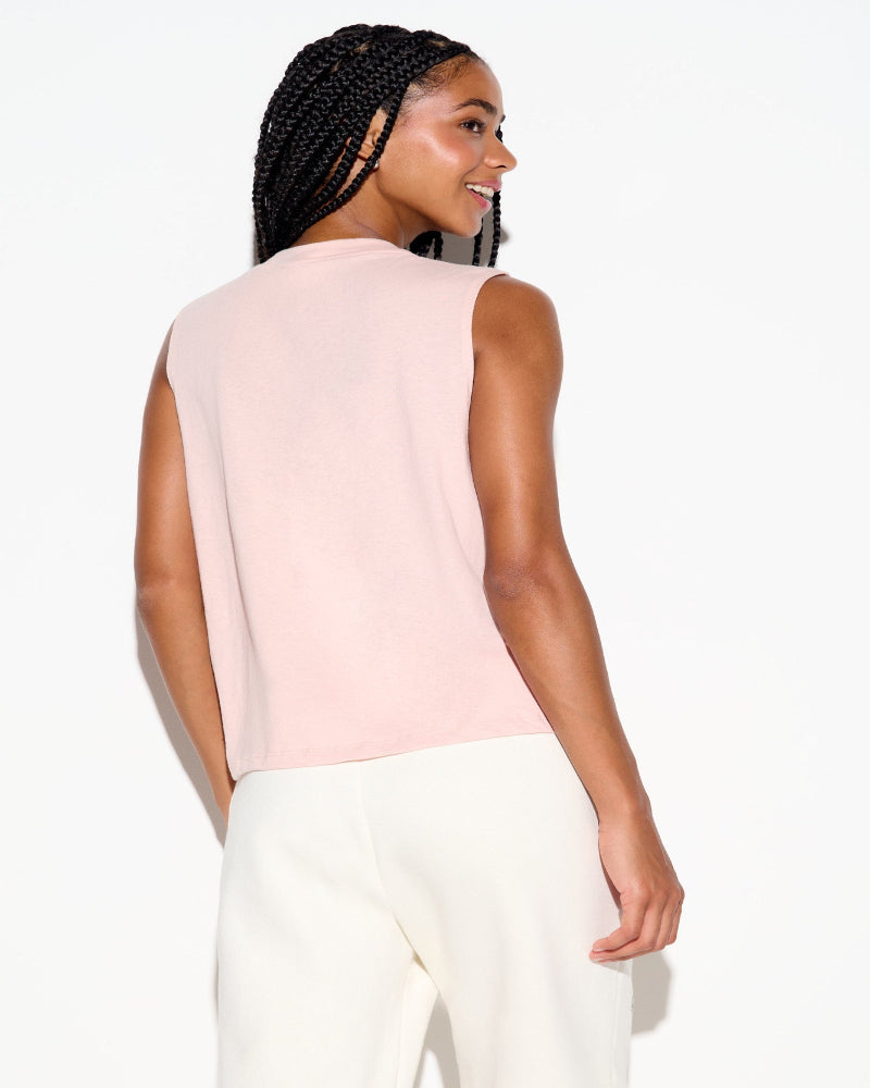 Woman wearing a light pink sleeveless top and white pants on a white background