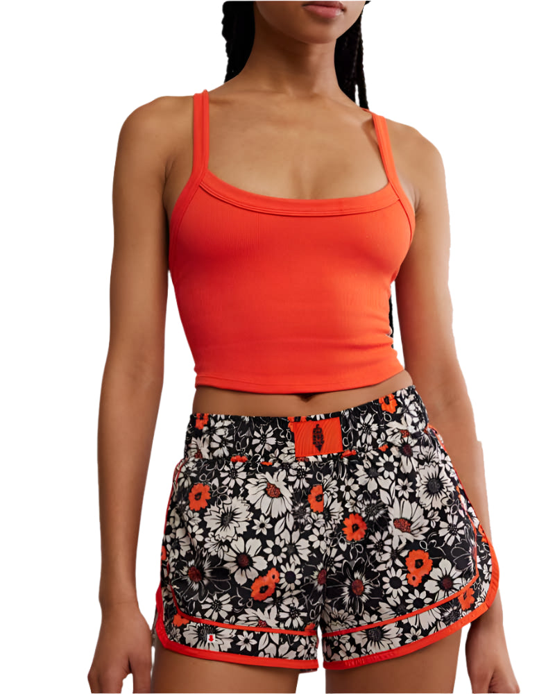 Woman wearing an orange crop top and floral shorts with a white background
