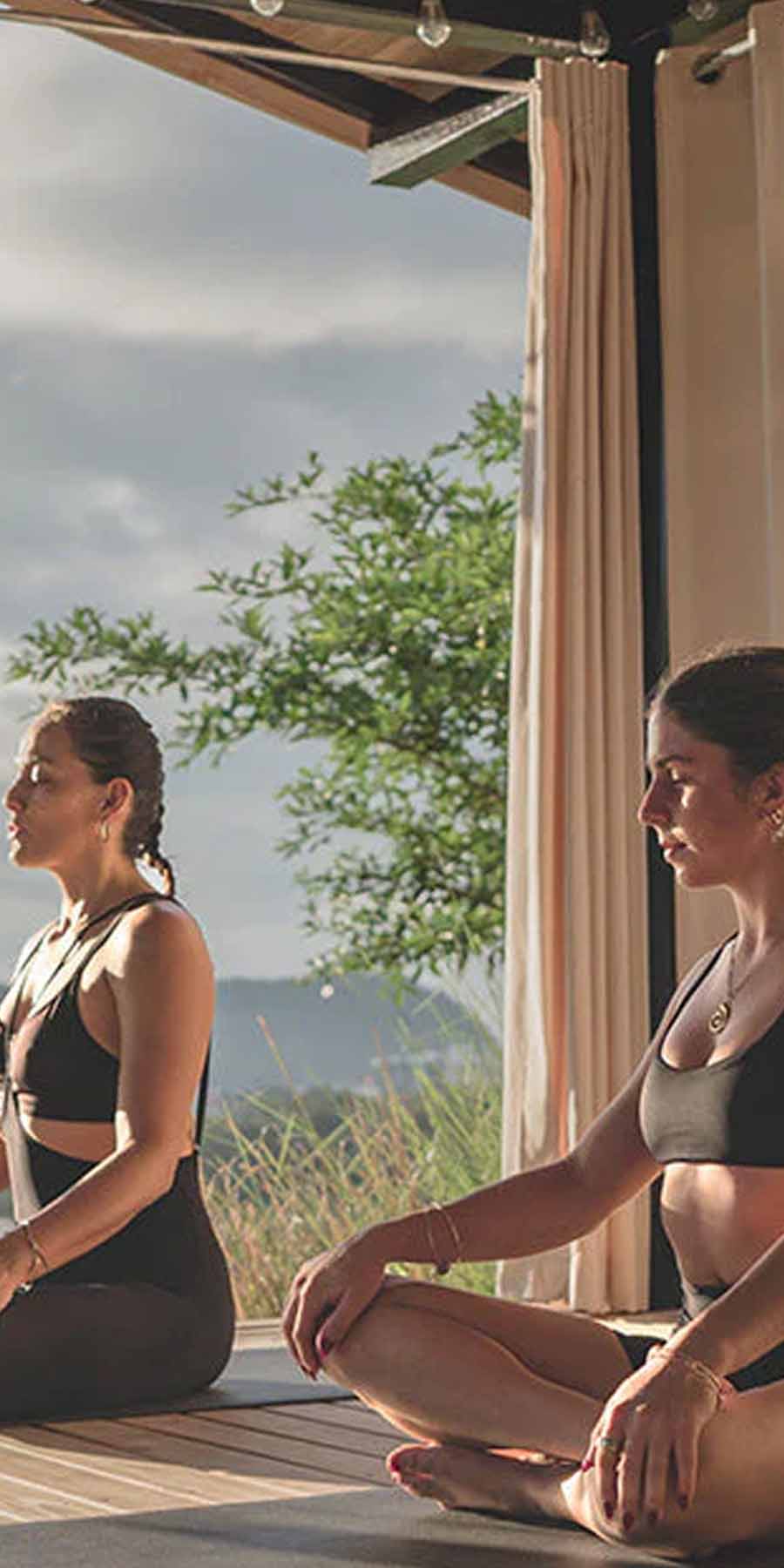 Two women practicing yoga outdoors with a scenic background