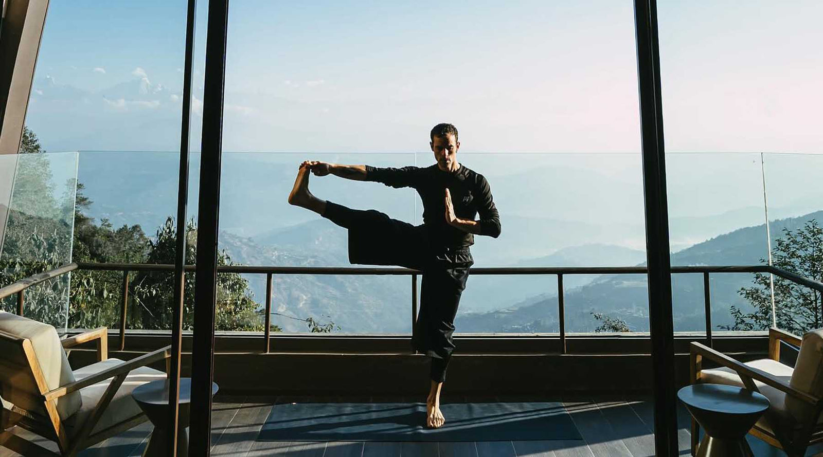 Person practicing yoga on a balcony with a scenic view of mountains