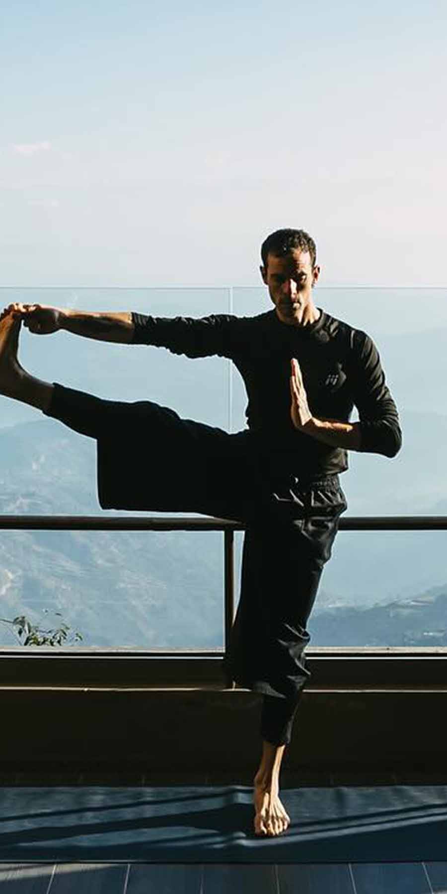 Person in black outfit performing a yoga pose with mountains in the background
